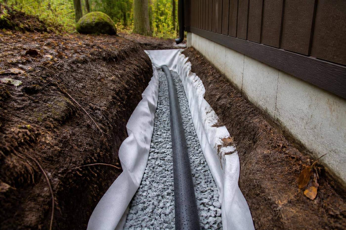 Weeping tile and clear stone in a drainage trench beside a cottage foundation