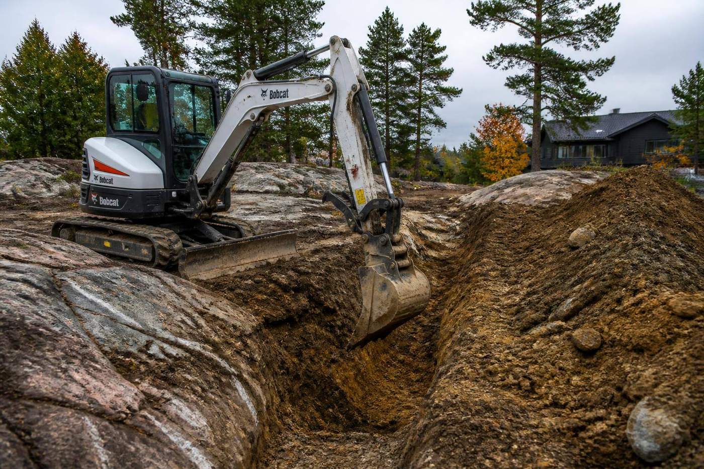 Compact excavator digging a foundation trench on a rocky Muskoka lot